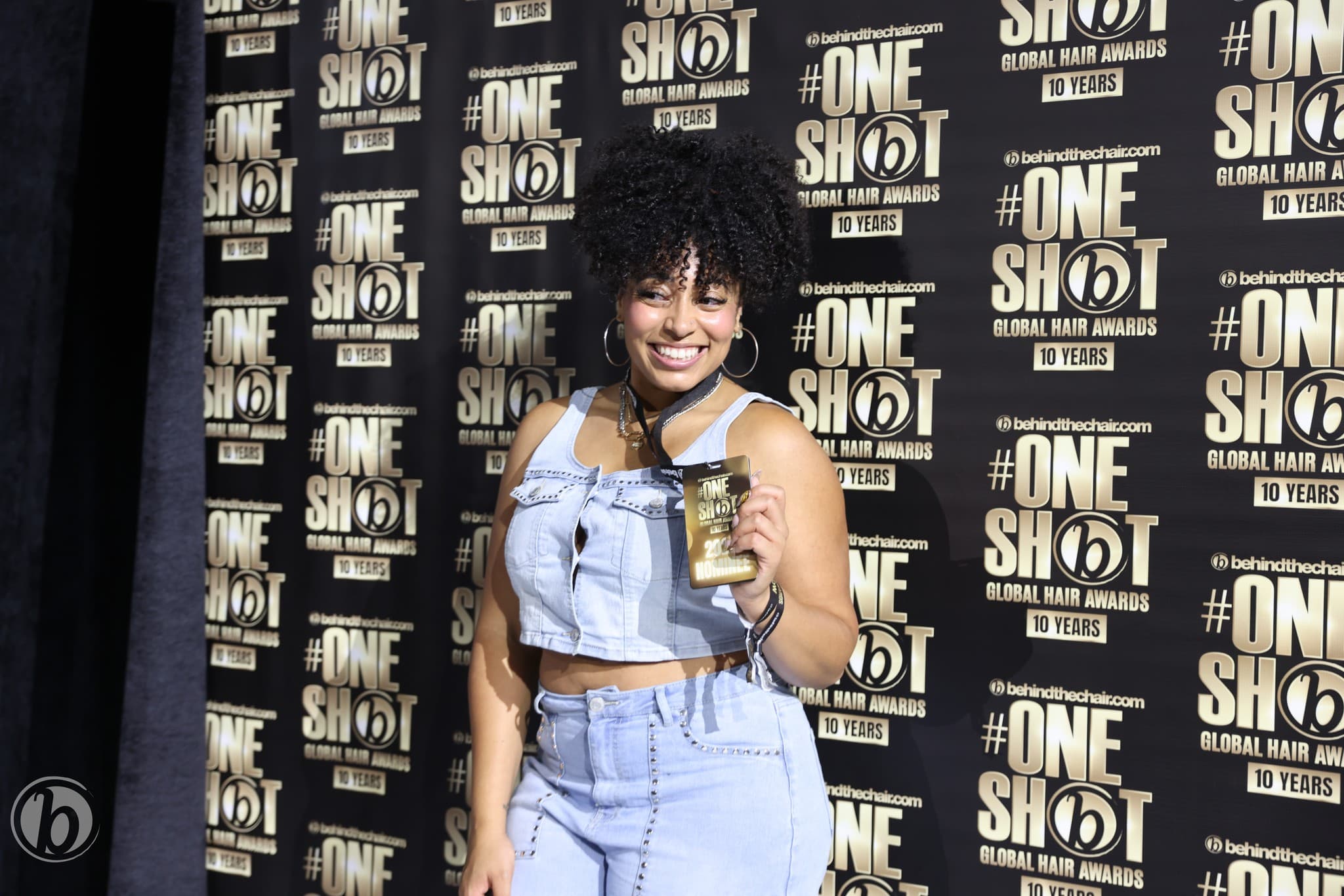 #ONESHOT nominee holding her TOP 100 badge on the step-and-repeat